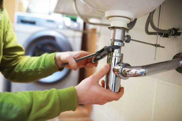 Plumber fixing a sink pipe with wrench.